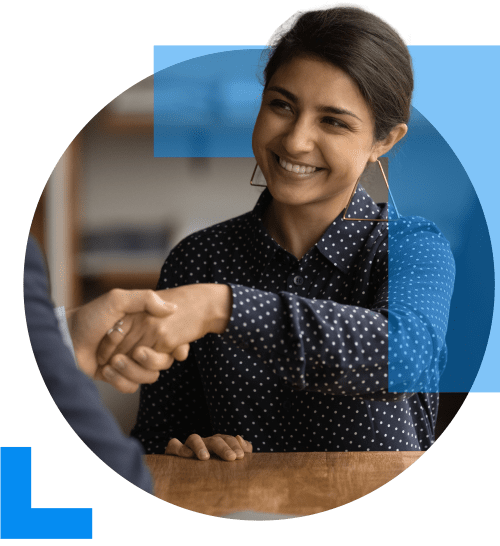 A woman shakes hands with another individual accross a table in an interview setting, representing the Recruitment sector.