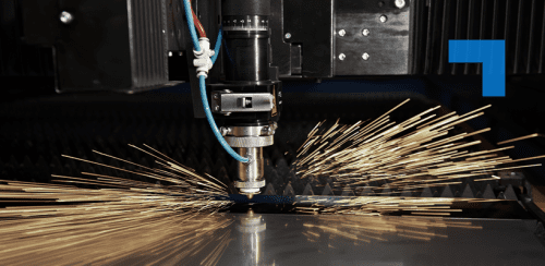 A laser cutting machine in operation, emitting bright golden sparks as it slices through a sheet of metal. The cutting head, surrounded by cables and mechanical parts, is the focal point against an industrial backdrop.