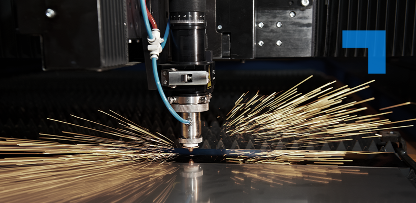 A laser cutting machine in operation, emitting bright golden sparks as it slices through a sheet of metal. The cutting head, surrounded by cables and mechanical parts, is the focal point against an industrial backdrop.