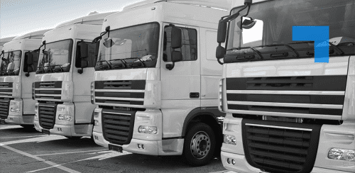 A row of five white semi-trucks parked closely together in a lot, all facing the same direction. Each truck features large windscreens, side mirrors, and prominent front grilles.