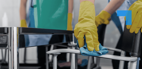 A person wearing yellow gloves cleaning a chair with a blue cloth.