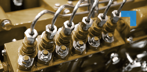 A close-up of industrial hydraulic fittings and metal pipes mounted on a gold-coloured machine component, showing precision-engineered connections in a manufacturing or engineering setting.