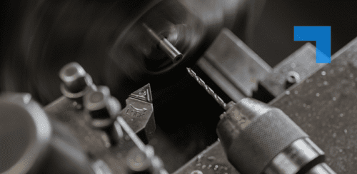 Close-up of precision machining equipment in operation, showing a rotating metal component on a lathe with a drill bit positioned nearby, illustrating high-precision manufacturing in an industrial engineering environment.