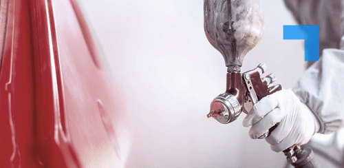 A person wearing PPC holds a paint spraying device to spray a red vehicle.