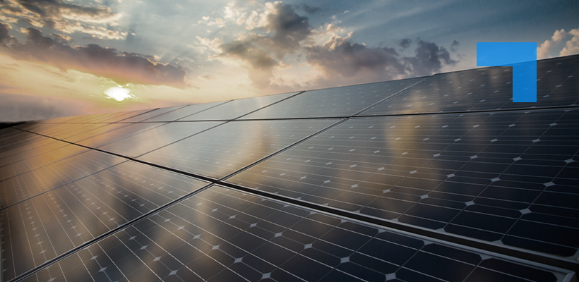 Solar panels arranged in rows under a partly cloudy sky at sunset, reflecting sunlight, with warm orange and blue tones across the scene.