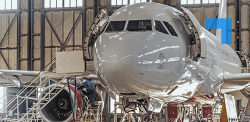 Front view of a commercial airplane inside a maintenance hangar, with its nose panels open and technicians working on equipment near the front landing gear and engine.
