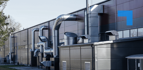 Industrial building exterior with large metal ventilation ducts and extraction systems mounted along the wall, illustrating commercial air handling infrastructure.