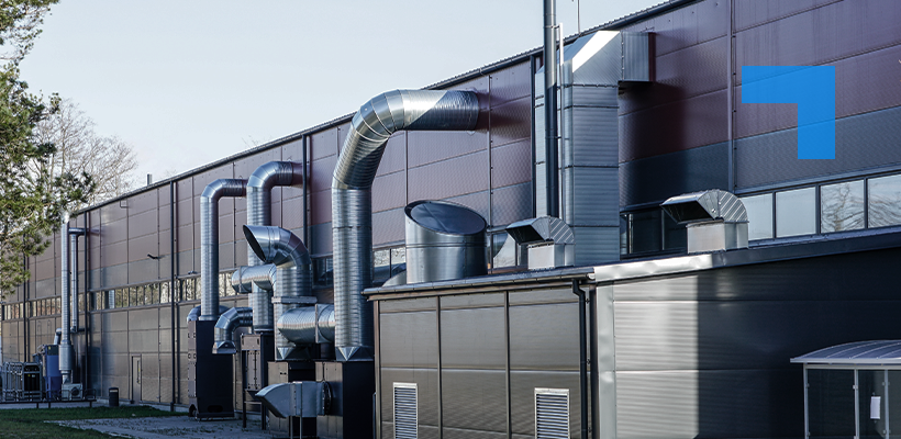Industrial building exterior with large metal ventilation ducts and extraction systems mounted along the wall, illustrating commercial air handling infrastructure.