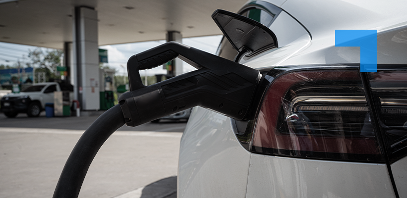 Electric vehicle charging cable plugged into a white car at a public charging station, symbolising EV infrastructure and electrification.