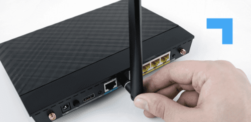 Close-up of a hand attaching an antenna to a black wireless router, showing the router's rear ports including Ethernet, USB, and power connections.
