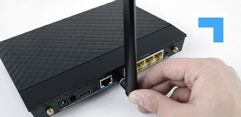 Close-up of a hand attaching an antenna to a black wireless router, showing the router's rear ports including Ethernet, USB, and power connections.