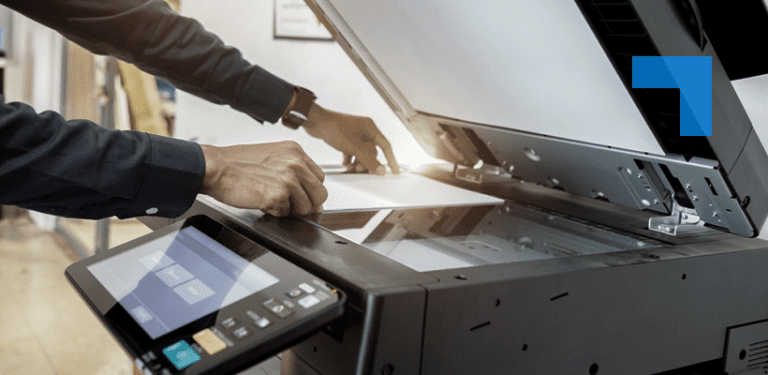 A person loads documents into a high-capacity office scanner or multifunction printer, illustrating document digitisation and records management services in a professional workplace setting.