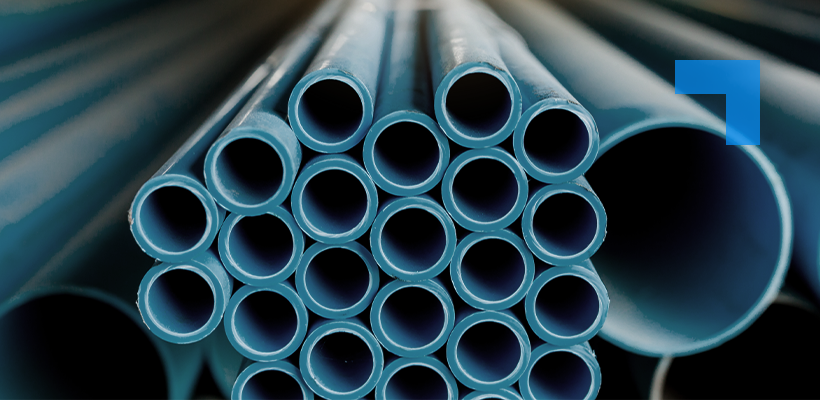 A close-up of stacked blue metal pipes of varying diameters, viewed from their open ends, with larger pipes blurred in the background.