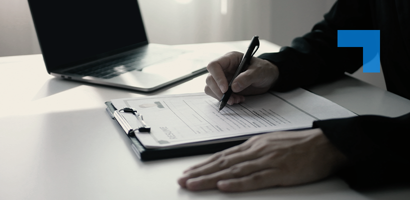 A person signing a recruitment document on a clipboard beside a laptop.