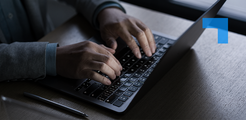 Close-up of a person typing on a laptop at a dark wooden desk, with a pen beside the computer.