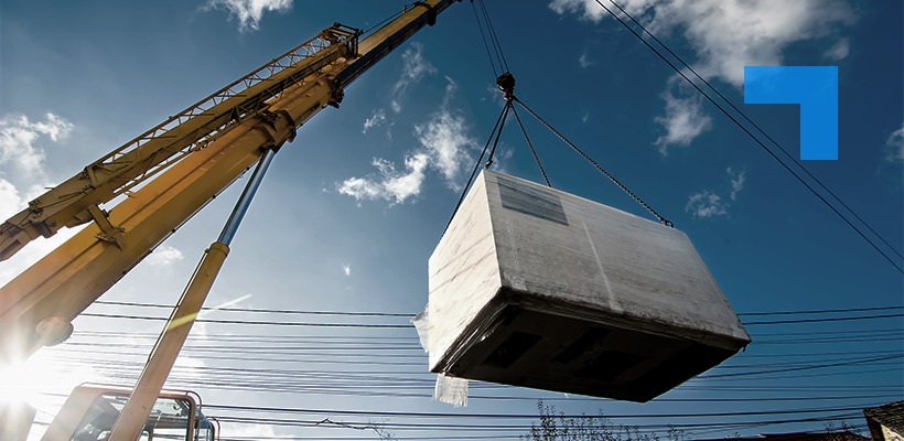 A yellow crane lifts a large piece of industrial equipment against a blue sky.