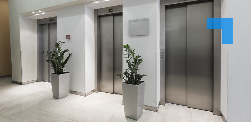 A modern commercial lift lobby featuring three stainless steel lift doors set against white walls, with potted plants between each door and a tiled floor.